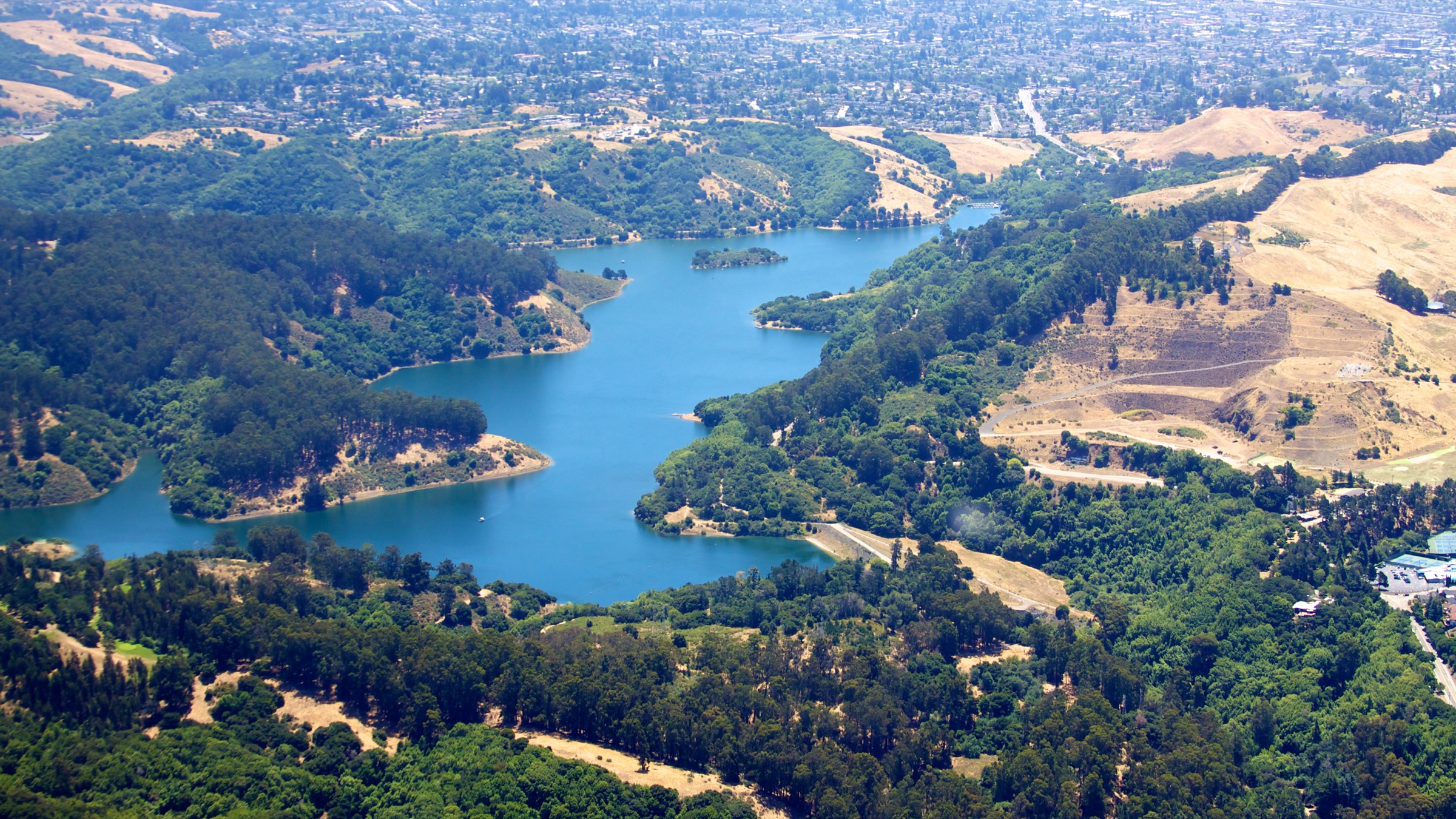 Aerial view of Lake Chabot in its wooded canyon, with the gold hills of Castro Valley beyond and San Leandro spread out to the horizon